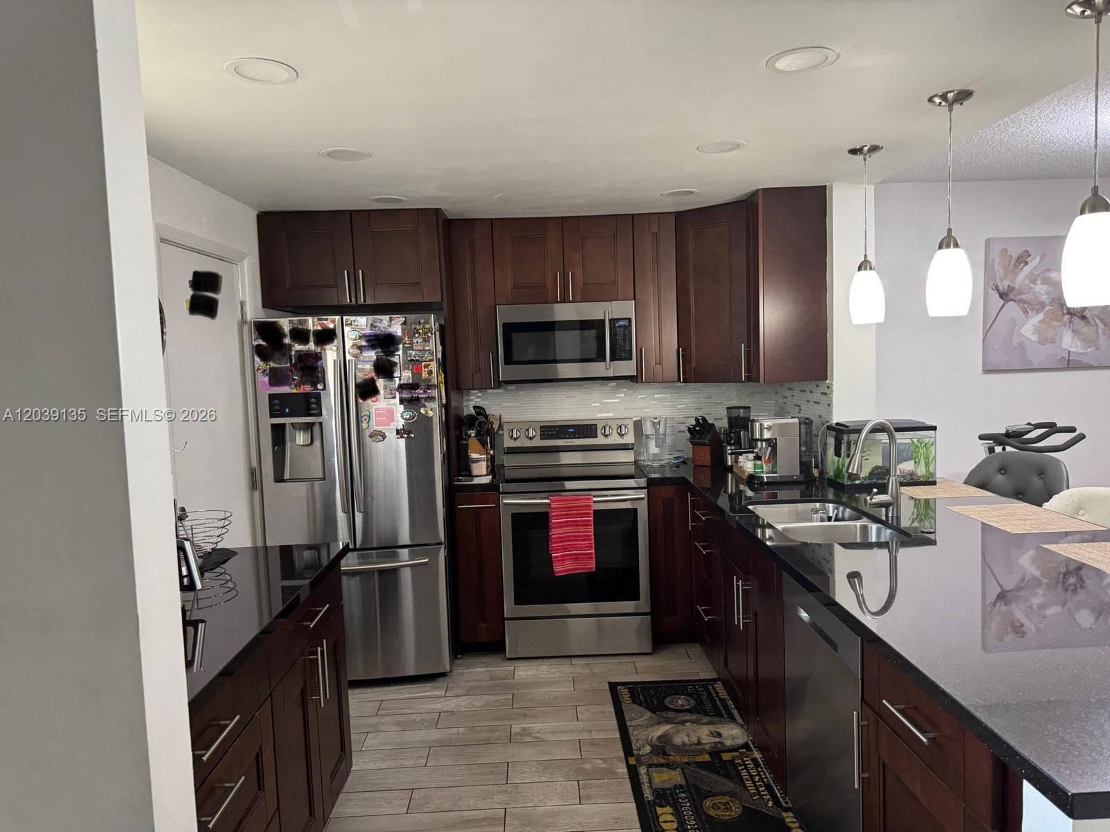 A kitchen features dark wood cabinets, stainless steel appliances, and black countertops — 900 NE 12th Ave # 302, Hallandale Beach FL 33009, HALLANDALE BEACH, FL