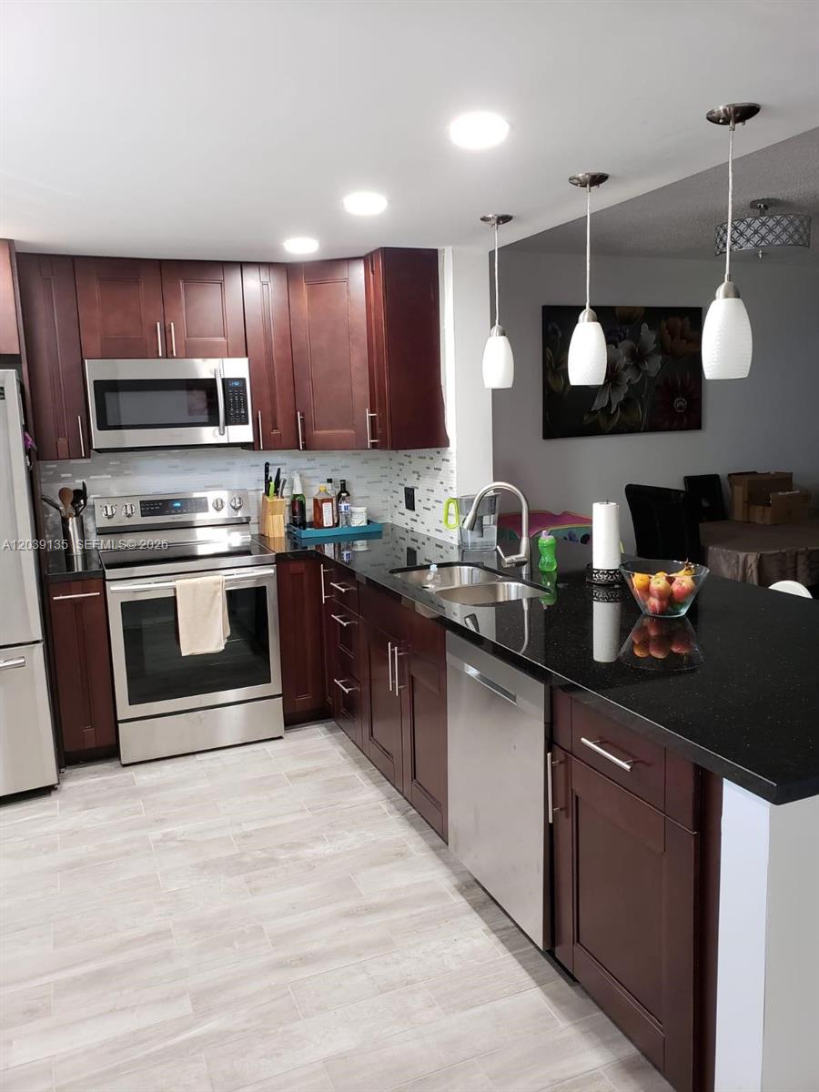 A kitchen features dark wood cabinets, black granite countertops, stainless steel appliances, and light flooring — 900 NE 12th Ave # 302, Hallandale Beach FL 33009, HALLANDALE BEACH, FL