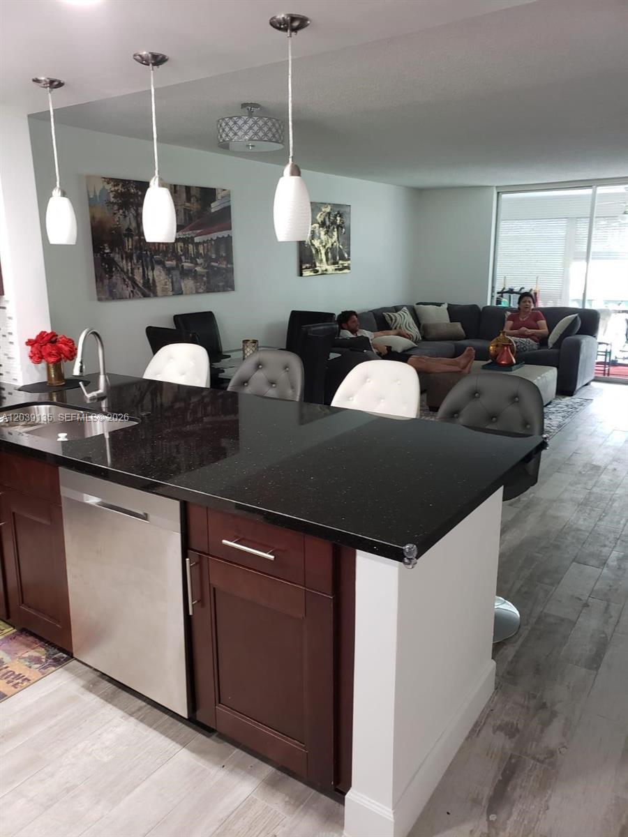 A kitchen island with a black countertop faces a living area with a sectional sofa — 900 NE 12th Ave # 302, Hallandale Beach FL 33009, HALLANDALE BEACH, FL