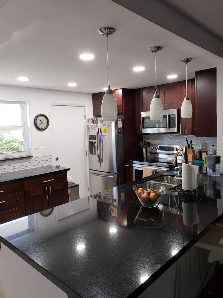 A kitchen features dark wood cabinets, black granite countertops, stainless steel appliances, and pendant lighting — 900 NE 12th Ave # 302, Hallandale Beach FL 33009, HALLANDALE BEACH, FL