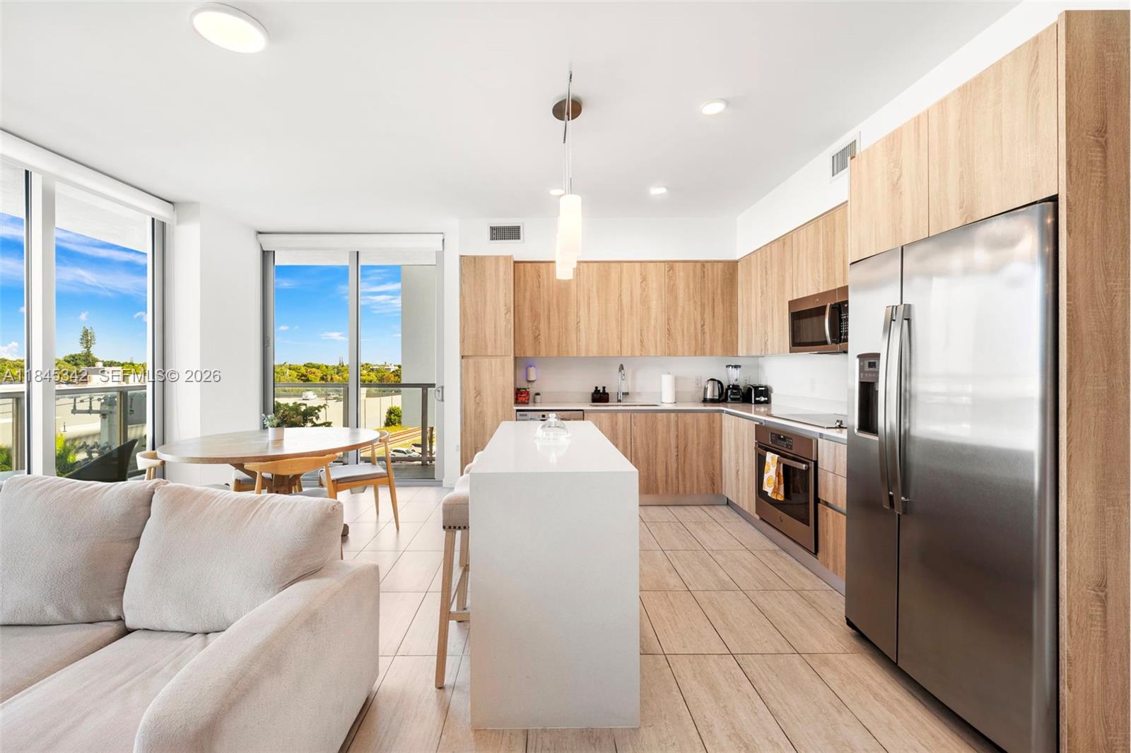 A modern kitchen features light wood cabinetry, a white island, and a dining area nearby — 3900 Biscayne Blvd # 400, Miami FL 33137, MIAMI, FL