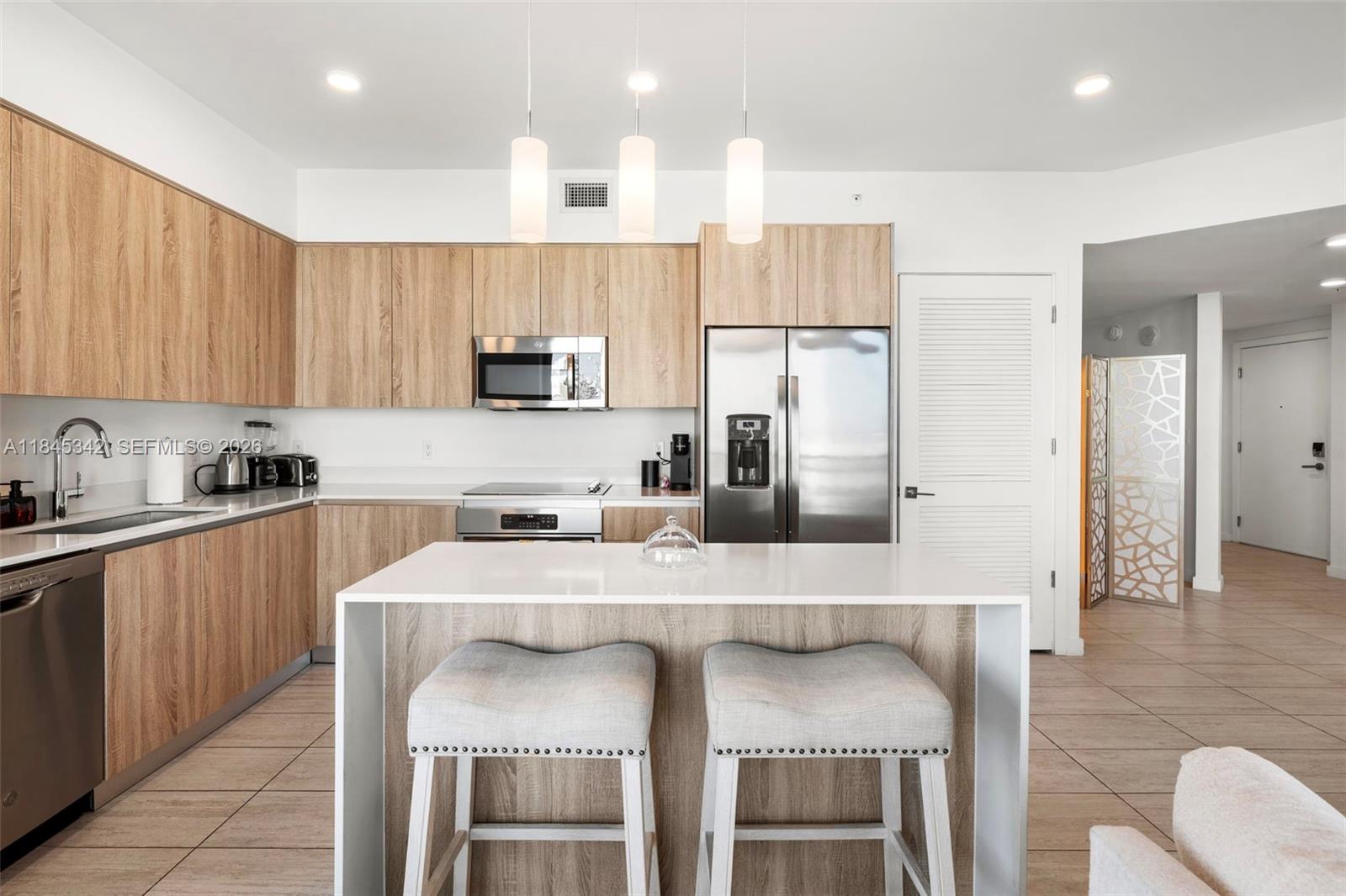 A modern kitchen features light wood cabinets, stainless steel appliances, and a white island — 3900 Biscayne Blvd # 400, Miami FL 33137, MIAMI, FL