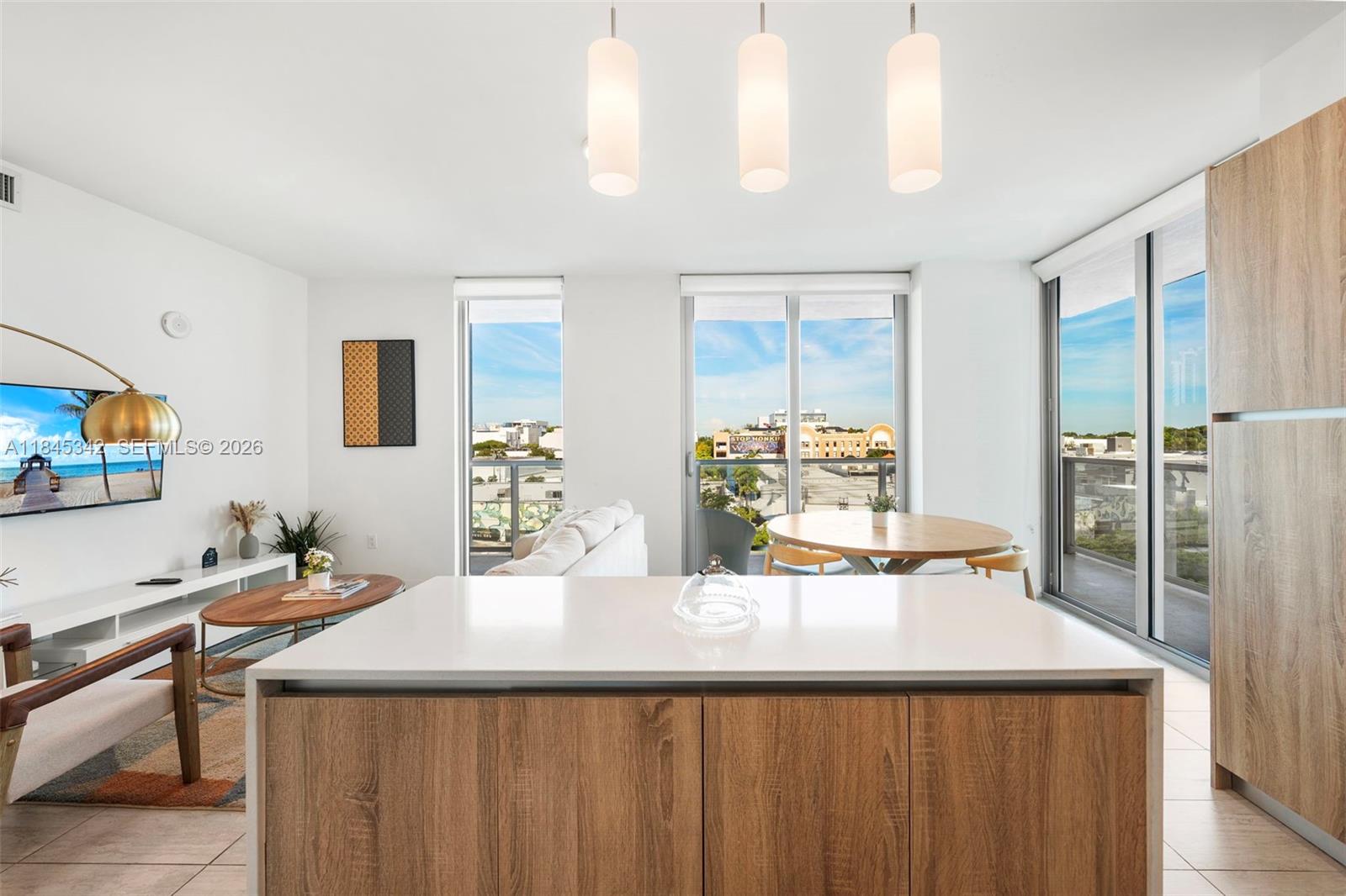 A modern kitchen island with wood cabinetry faces a living and dining area with balconies — 3900 Biscayne Blvd # 400, Miami FL 33137, MIAMI, FL