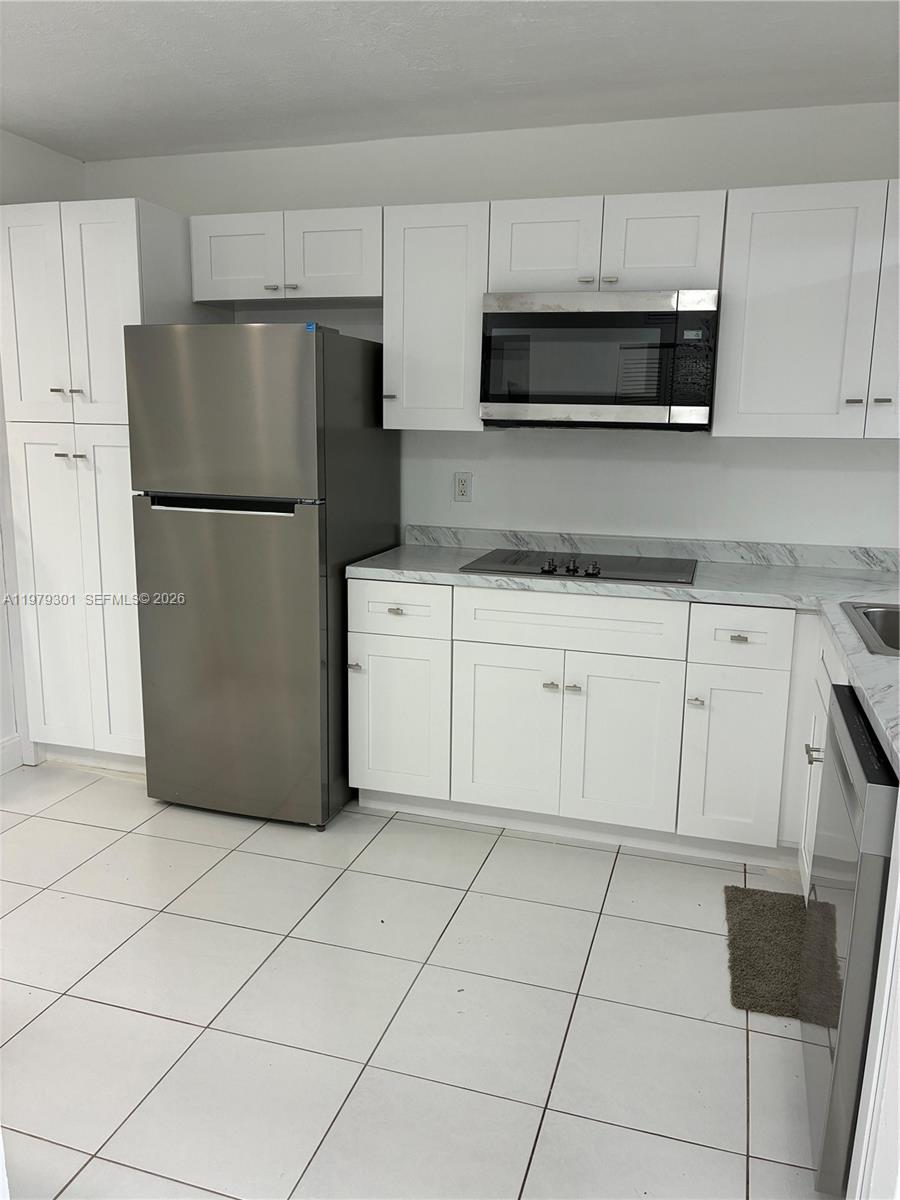 A kitchen features white cabinets, stainless steel appliances, and light-colored tile flooring — 609 S State Road 7 # 2C, Margate FL 33068, MARGATE, FL
