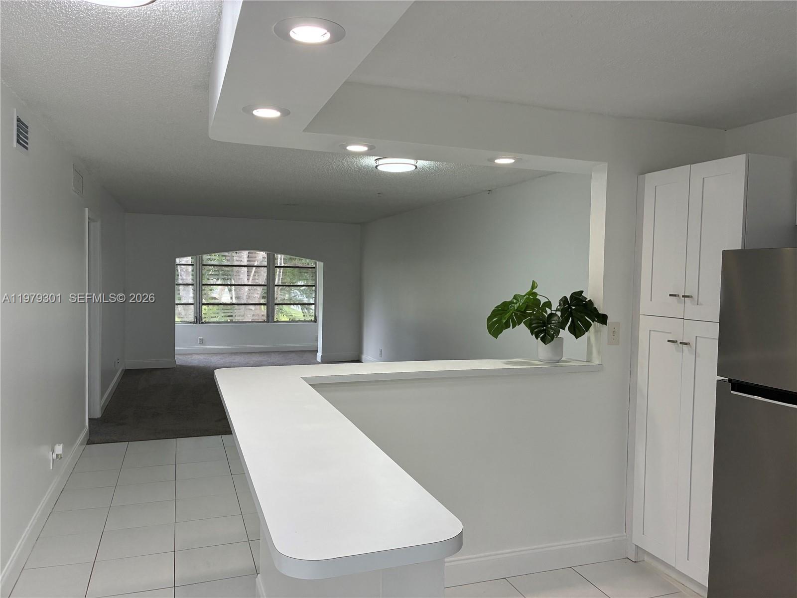 A kitchen with a white breakfast bar overlooks a living area with carpeted floors — 609 S State Road 7 # 2C, Margate FL 33068, MARGATE, FL
