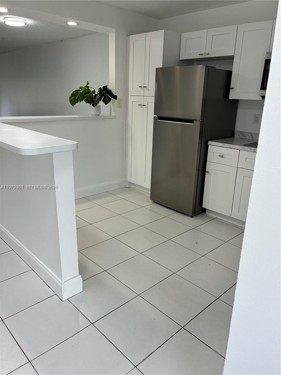 A kitchen features white cabinets, a stainless steel refrigerator, and white tile flooring — 609 S State Road 7 # 2C, Margate FL 33068, MARGATE, FL