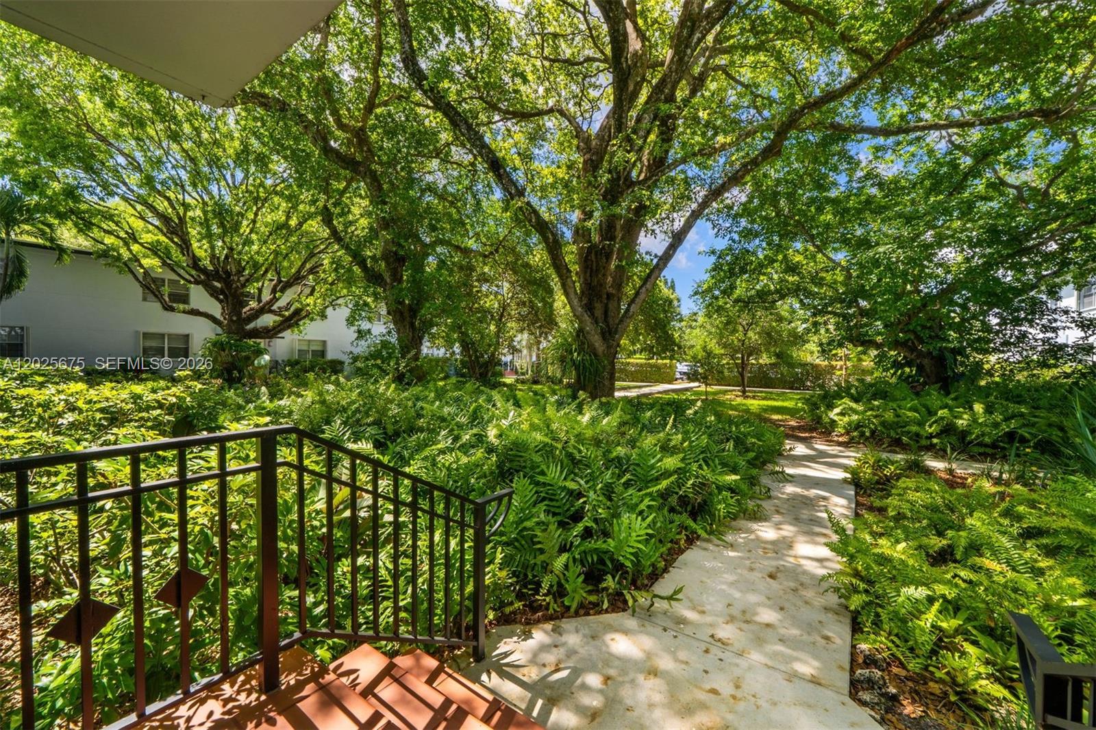 A concrete walkway leads through a lush, tree-filled garden past a set of outdoor stairs — 5605 SW 80th St # 10D, Miami FL 33143, MIAMI, FL