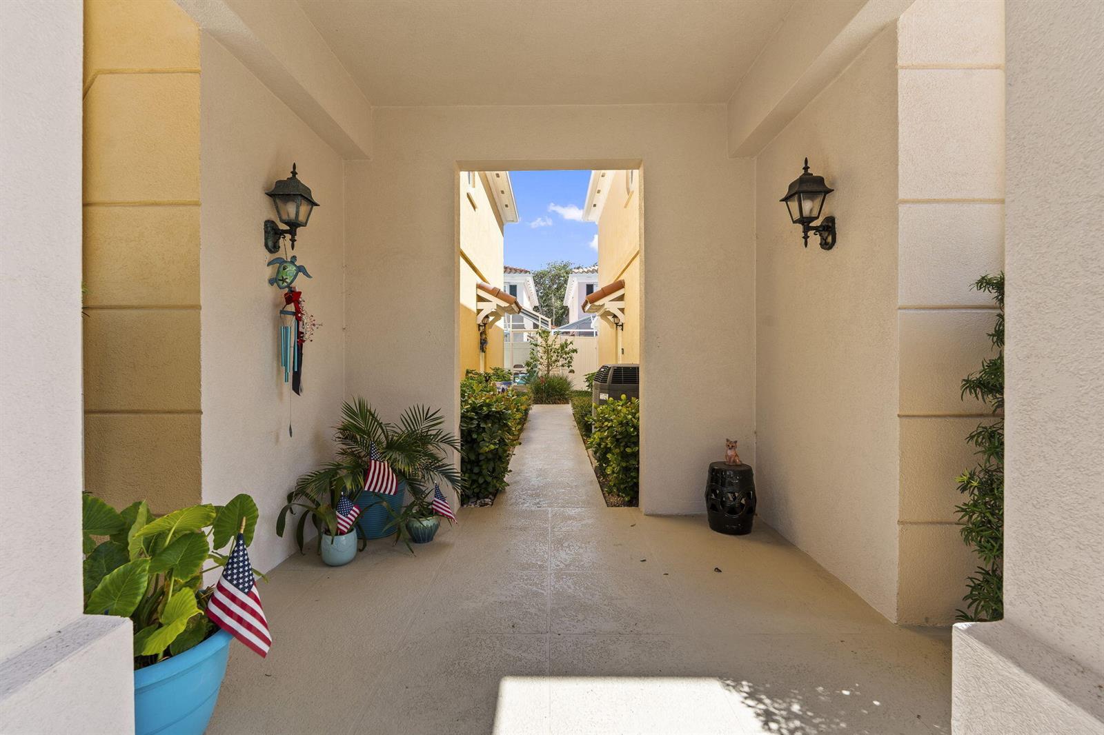 A covered entryway leads to a narrow outdoor walkway between two light-colored residential buildings — 48 Live Oak Circle, Jupiter FL 33469, JUPITER, FL
