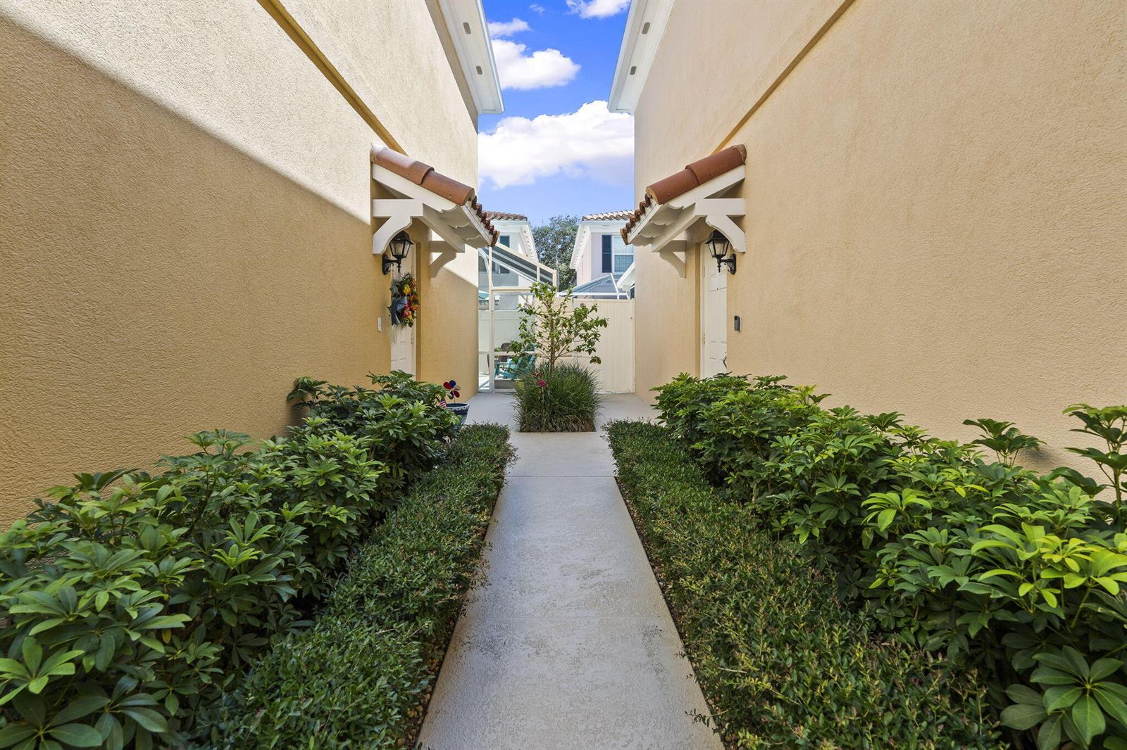 A concrete walkway leads between two tan stucco buildings with small tiled awnings and landscaping — 48 Live Oak Circle, Jupiter FL 33469, JUPITER, FL