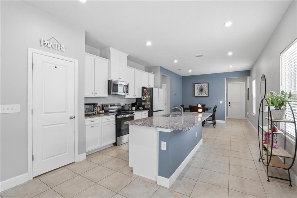 A kitchen features white cabinets, granite countertops, a blue island, and a pantry door — 8728 STARRY NIGHT TERRACE, PARRISH, FL