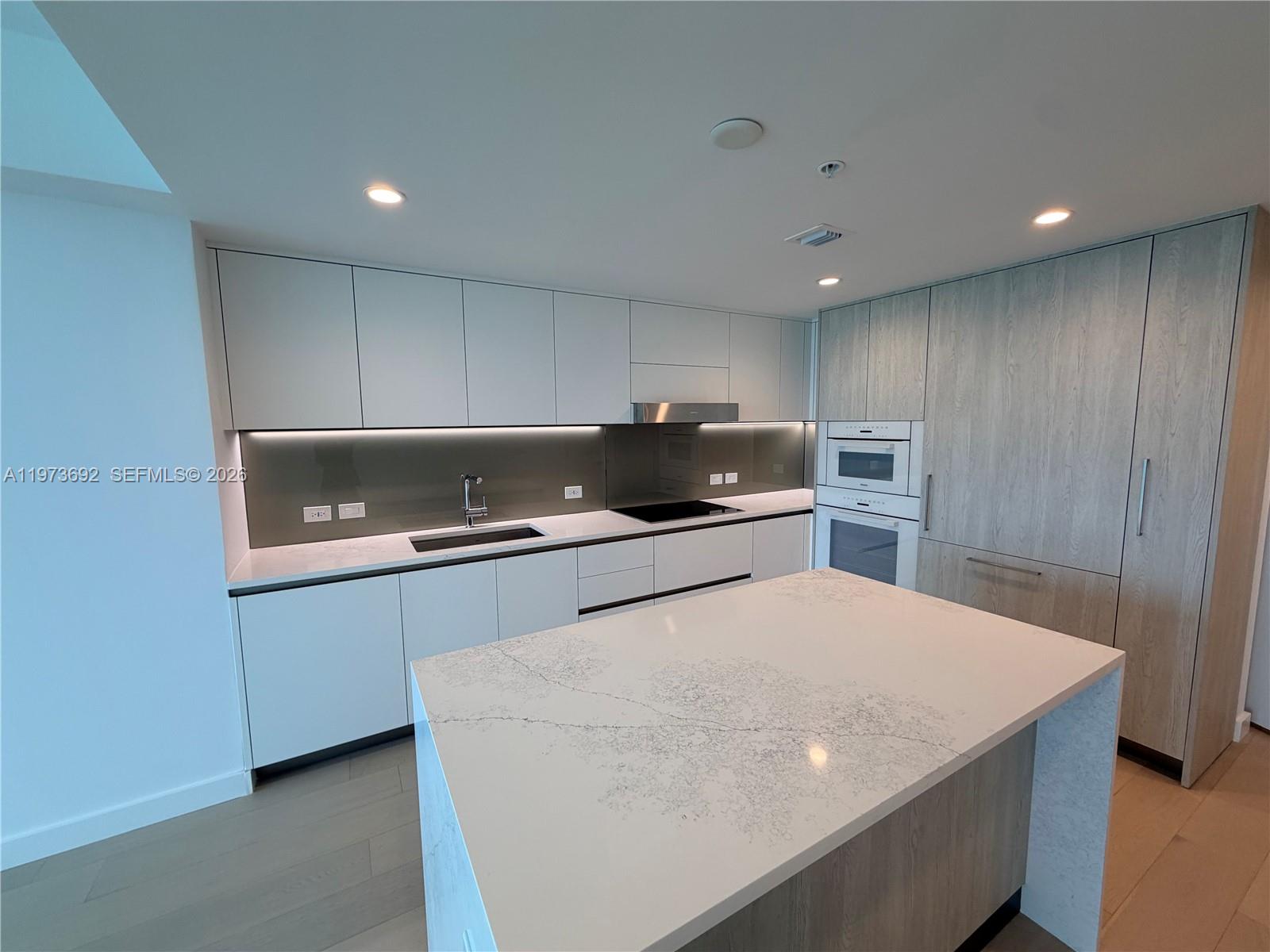 A modern kitchen features white cabinetry, a marble-topped island, and light wood-paneled appliances — 9221 E Bay Harbor Dr # 307, Bay Harbor Islands FL 33154, BAY HARBOR ISLANDS, FL