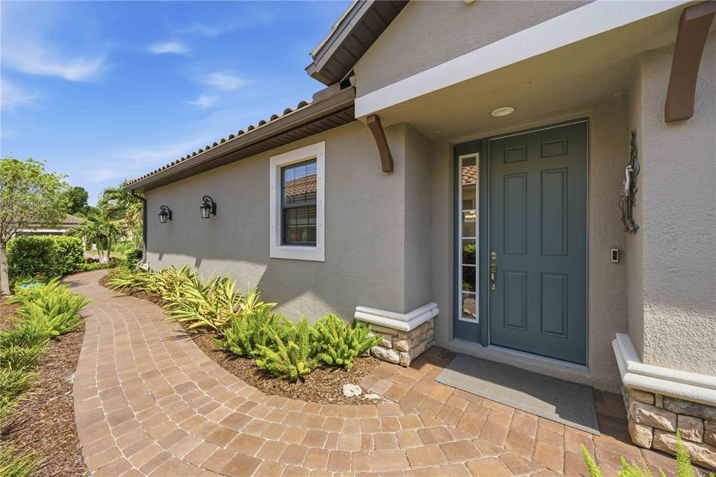 A paved walkway leads to the front entrance of a house with a blue door — 5749 SEMOLINO STREET, NOKOMIS, FL