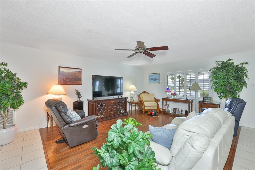 A living room features a white sofa, a leather recliner, wood flooring, and a television console — 684 ALLEGHENY DRIVE, SUN CITY CENTER, FL
