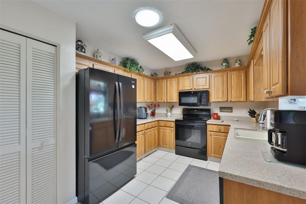 A kitchen features light wood cabinets, black appliances, white tile flooring, and speckled countertops — 684 ALLEGHENY DRIVE, SUN CITY CENTER, FL