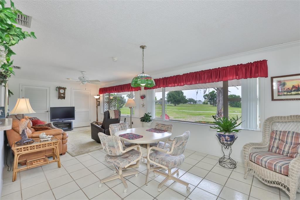 A living and dining area with tile floors, a round table, and large windows overlooking grass — 684 ALLEGHENY DRIVE, SUN CITY CENTER, FL