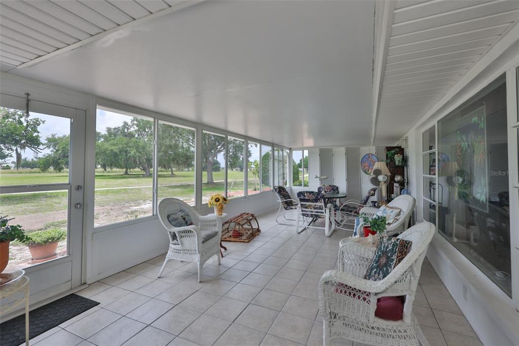 A sunroom with white wicker furniture, tile flooring, and large windows overlooking a grassy field — 684 ALLEGHENY DRIVE, SUN CITY CENTER, FL