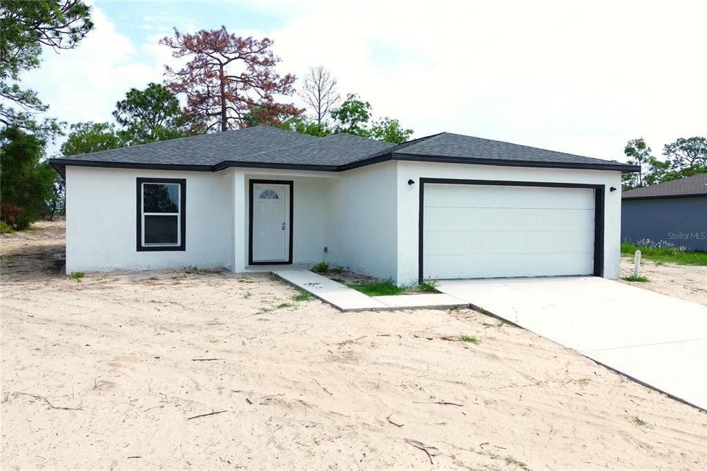 A white, single-story house with a two-car garage sits on a sandy, undeveloped lot — 12493 KILLIAN STREET, SPRING HILL, FL