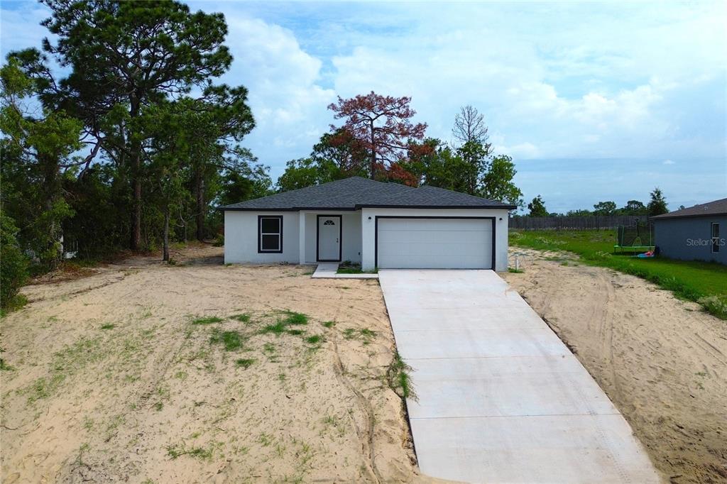 A single-story house with a white exterior, a two-car garage, and a sandy front yard — 12493 KILLIAN STREET, SPRING HILL, FL