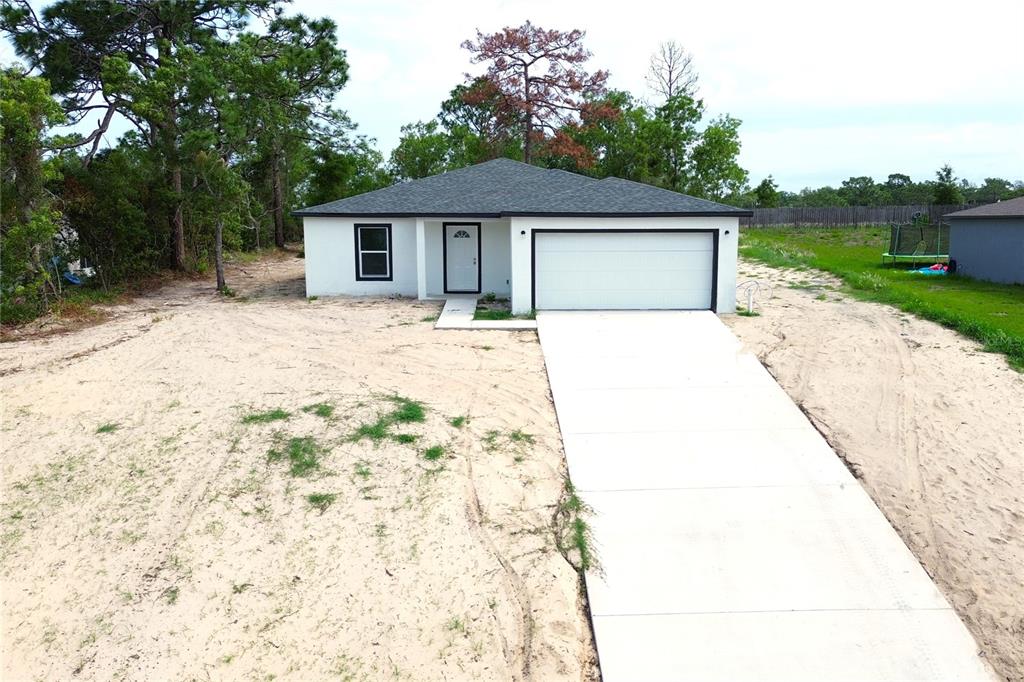 A single-story house with a white exterior, dark roof, and concrete driveway on a sandy lot — 12493 KILLIAN STREET, SPRING HILL, FL