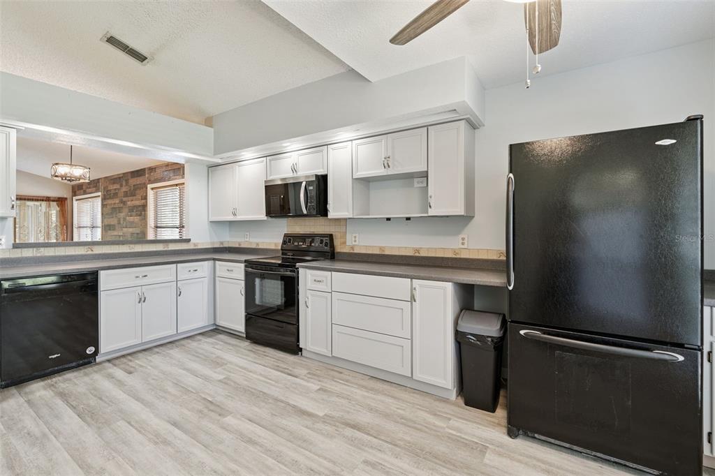 A kitchen features white cabinets, black appliances, gray countertops, and light wood-look flooring — 5526 DEEPDALE DRIVE, ORLANDO, FL