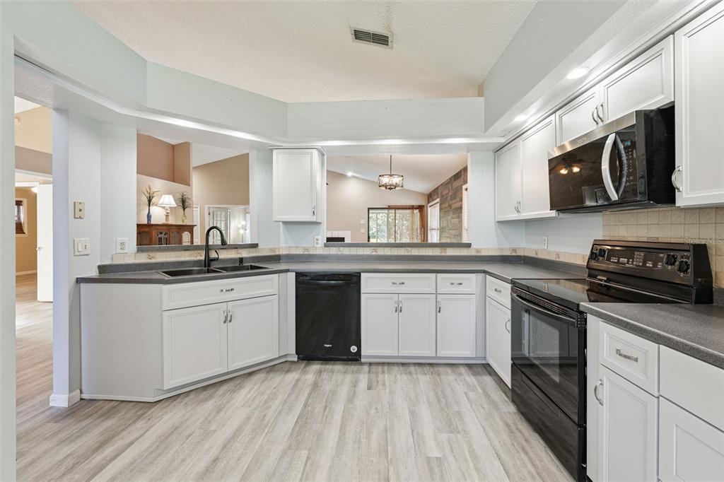 A kitchen with white cabinets, dark countertops, black appliances, and light wood-look flooring — 5526 DEEPDALE DRIVE, ORLANDO, FL