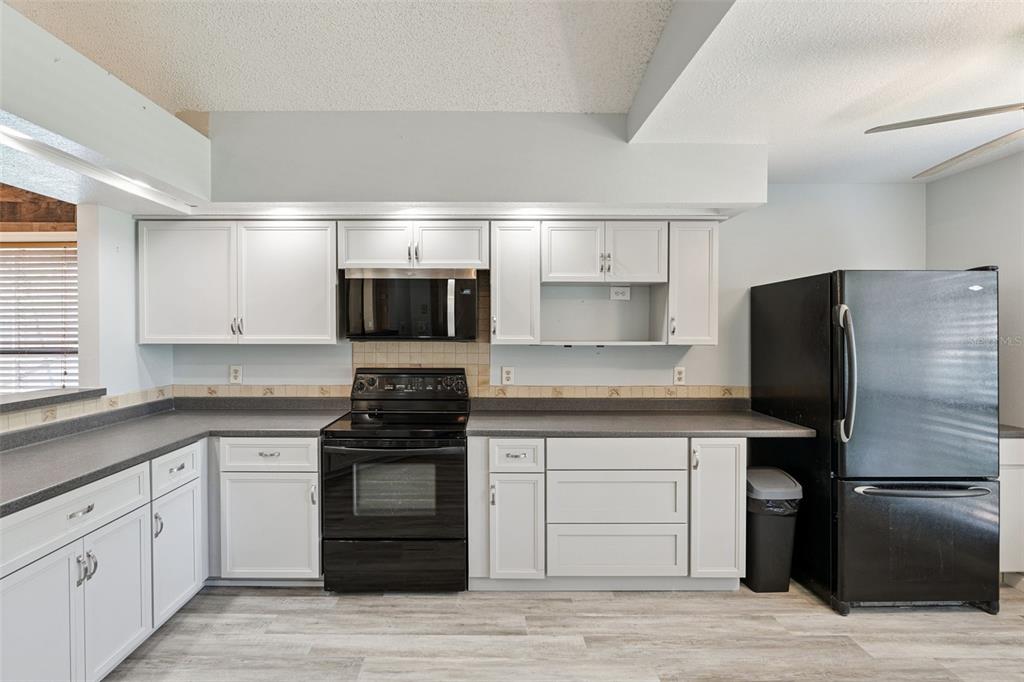 A kitchen features white cabinets, dark countertops, black appliances, and light wood-look flooring — 5526 DEEPDALE DRIVE, ORLANDO, FL
