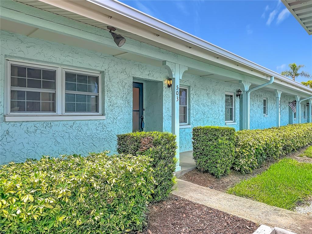 A light blue stucco building exterior features a covered walkway, green hedges, and windows — 2465 NORTHSIDE DR UNIT 503, CLEARWATER, FL