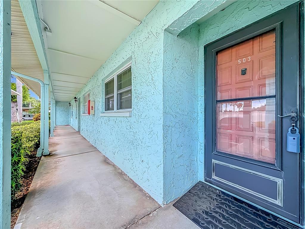 A light blue stucco building exterior features a covered walkway and a front door labeled 503 — 2465 NORTHSIDE DR UNIT 503, CLEARWATER, FL