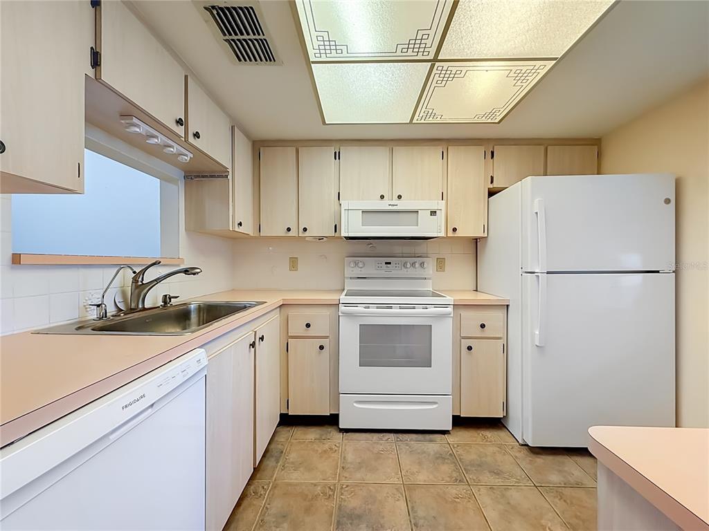 A kitchen features light wood cabinets, white appliances, pink countertops, and a tiled floor — 2465 NORTHSIDE DR UNIT 503, CLEARWATER, FL