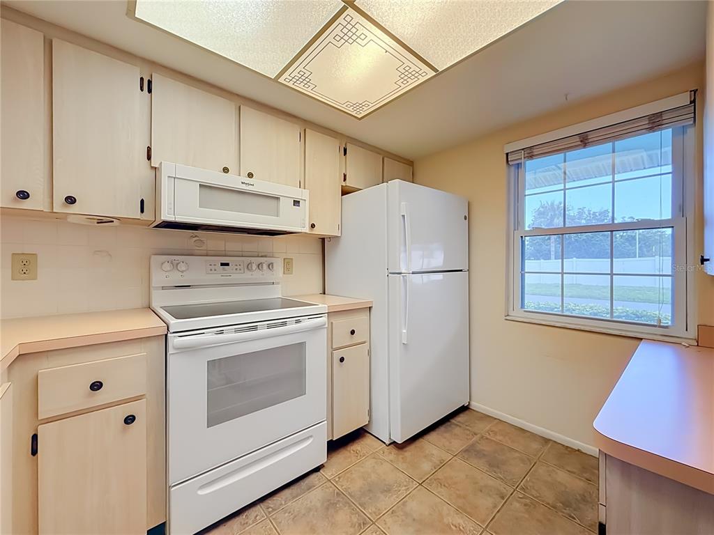 A kitchen features light wood cabinets, white appliances, laminate countertops, and a square ceiling light — 2465 NORTHSIDE DR UNIT 503, CLEARWATER, FL