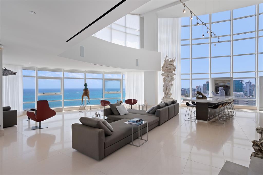 A modern living room with white floors, large windows, and panoramic ocean views — 1052 ASHFORD AVENUE UNIT PH-18, SAN JUAN, PR