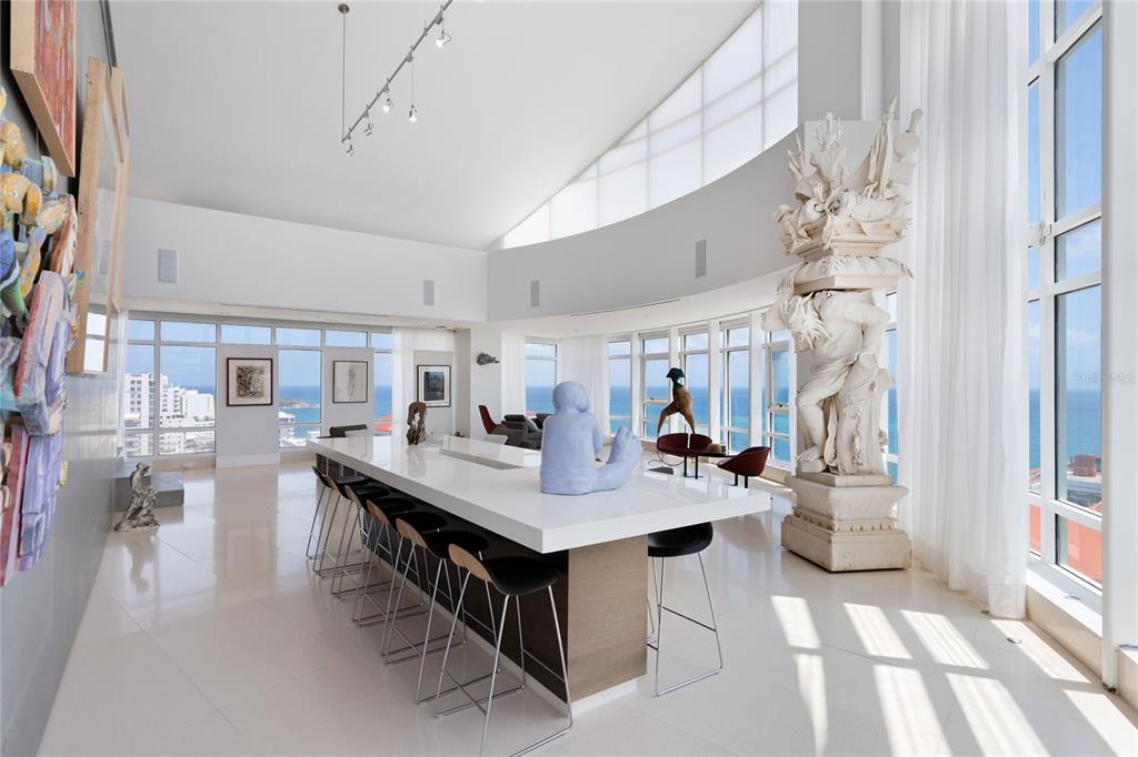 A bright room with white floors, two red chairs, modern art, and floor-to-ceiling ocean views — 1052 ASHFORD AVENUE UNIT PH-18, SAN JUAN, PR