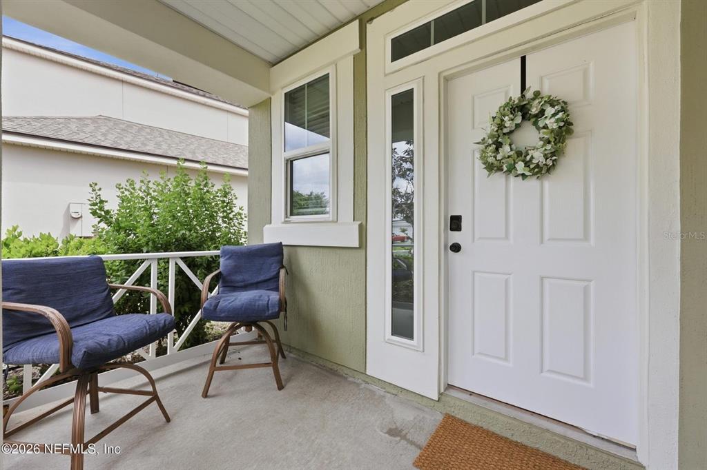 A covered front porch features two blue chairs, a white door with a wreath, and siding — 14589 GARDEN GATE DRIVE, JACKSONVILLE, FL