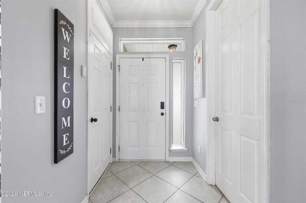 A bright entryway features a white front door, tiled flooring, and a vertical welcome sign — 14589 GARDEN GATE DRIVE, JACKSONVILLE, FL