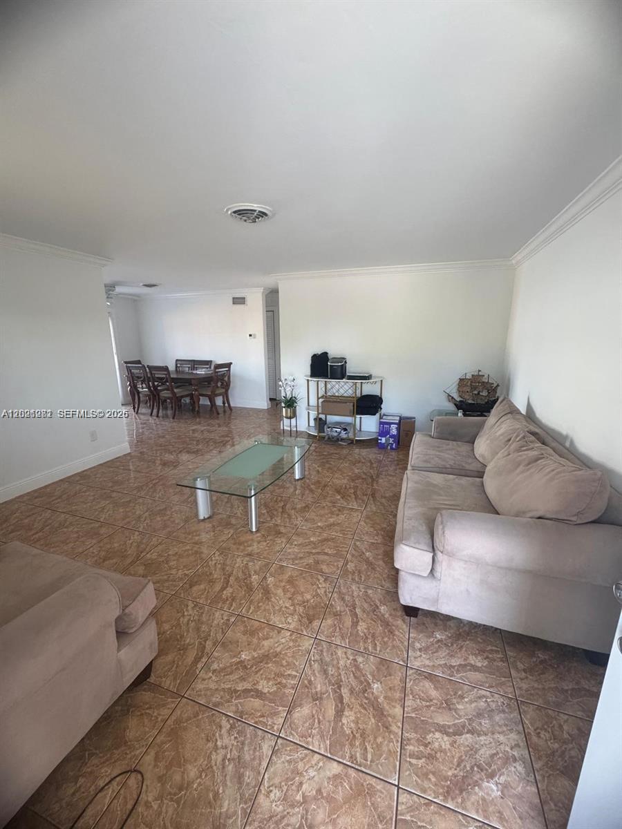 A living room with beige sofas, a glass coffee table, and tile flooring leads to a dining area — 2801 NW 183rd St, Miami Gardens FL 33056, MIAMI GARDENS, FL
