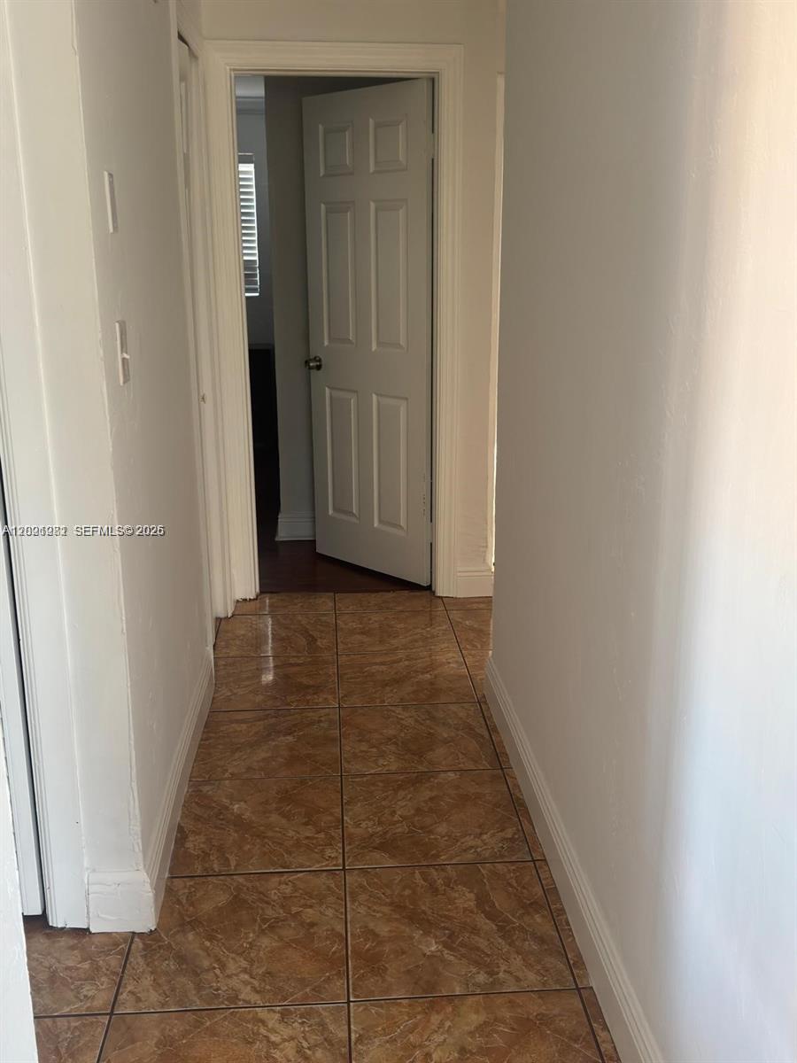 A hallway with brown marble-patterned tile flooring leads to an open white interior door — 2801 NW 183rd St, Miami Gardens FL 33056, MIAMI GARDENS, FL