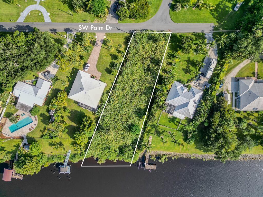 An aerial view shows a vacant, rectangular waterfront lot situated between two existing residential properties — 15340 SW Palm Drive, FL 34956, FL