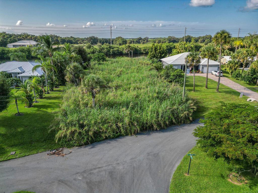 An aerial view shows a vacant, overgrown lot situated between two residential houses and a canal — 15340 SW Palm Drive, FL 34956, FL