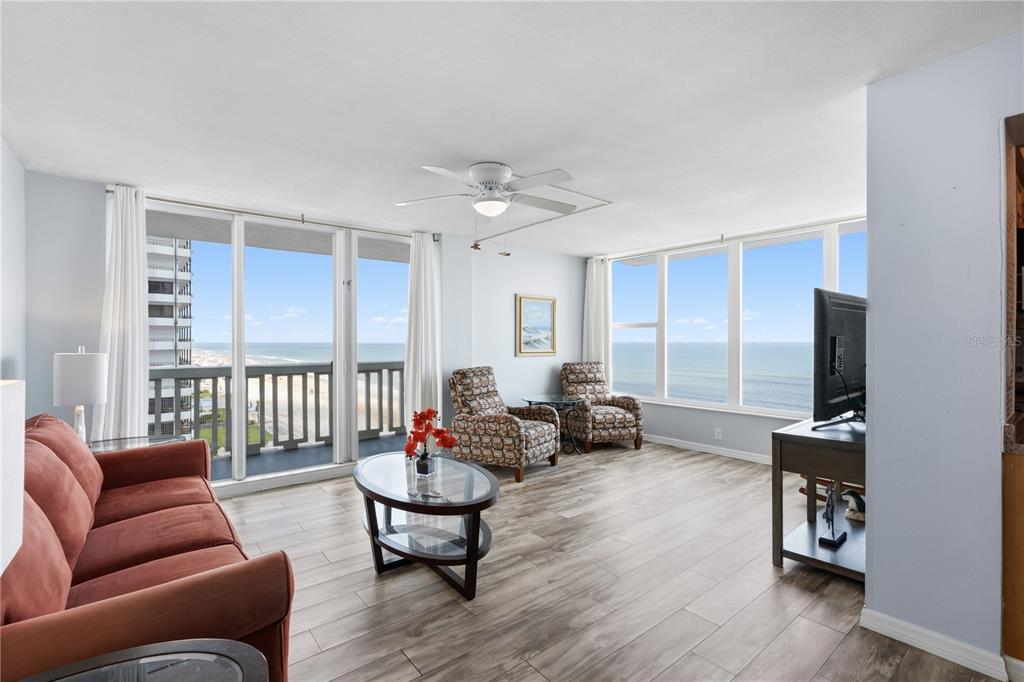 A living room with wood-look tile flooring, a red sofa, and floor-to-ceiling ocean views — 2800 N ATLANTIC AVENUE UNIT 715, DAYTONA BEACH, FL