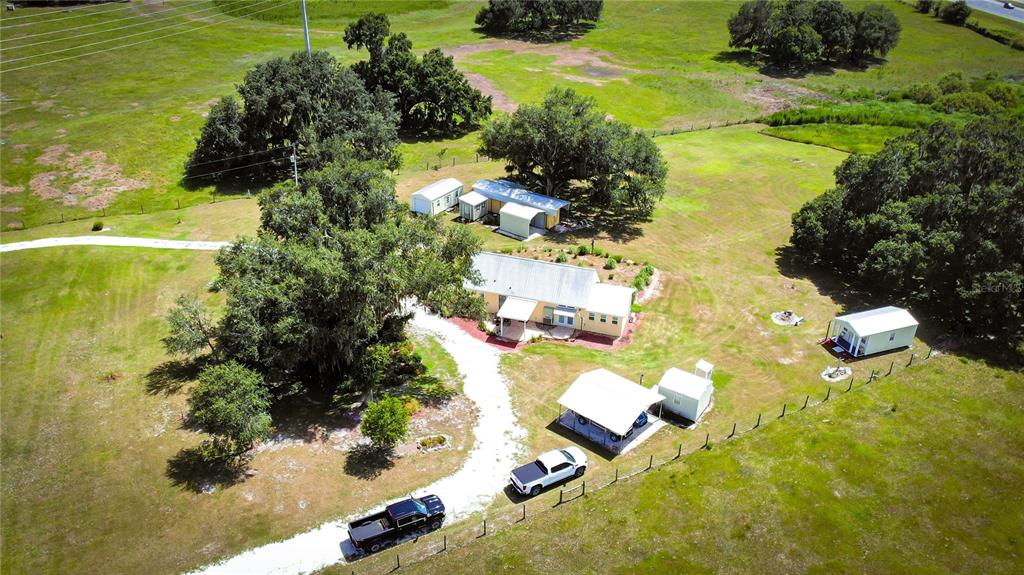 An aerial view shows a rural property with a house, several outbuildings, and two parked trucks — 7820 SW 32ND STREET, BUSHNELL, FL
