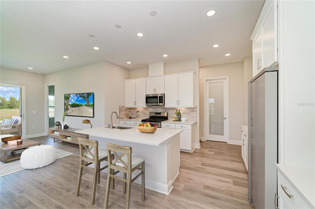 A modern kitchen with white cabinets, a central island, and wood-look flooring opens to a living area — 35509 STABLETON LANE, ZEPHYRHILLS, FL