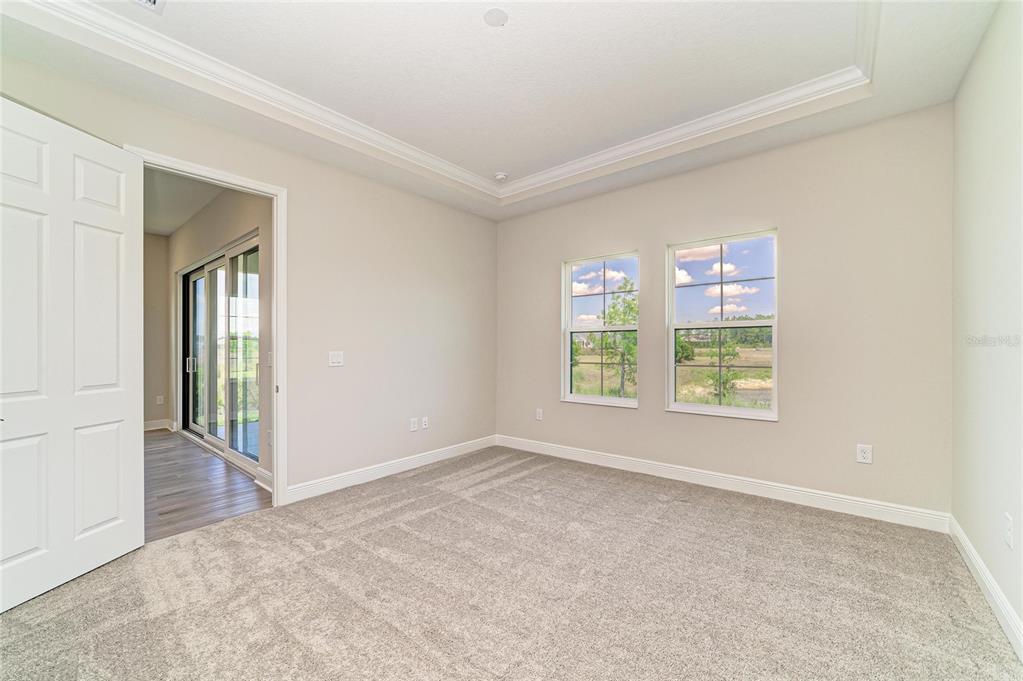 An empty bedroom features neutral walls, gray carpeting, a tray ceiling, and sliding glass doors — 35509 STABLETON LANE, ZEPHYRHILLS, FL