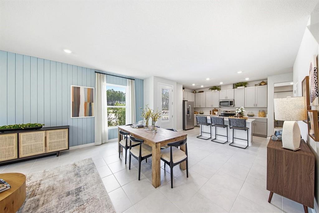 A dining area with a wood table and blue paneled wall opens to a modern kitchen — 1140 WILD CREST LANE, DAYTONA BEACH, FL