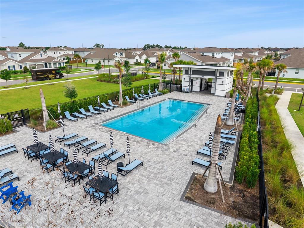 An outdoor community swimming pool surrounded by lounge chairs, tables with umbrellas, and landscaping — 19053 BLUELEAF STREET, ORLANDO, FL