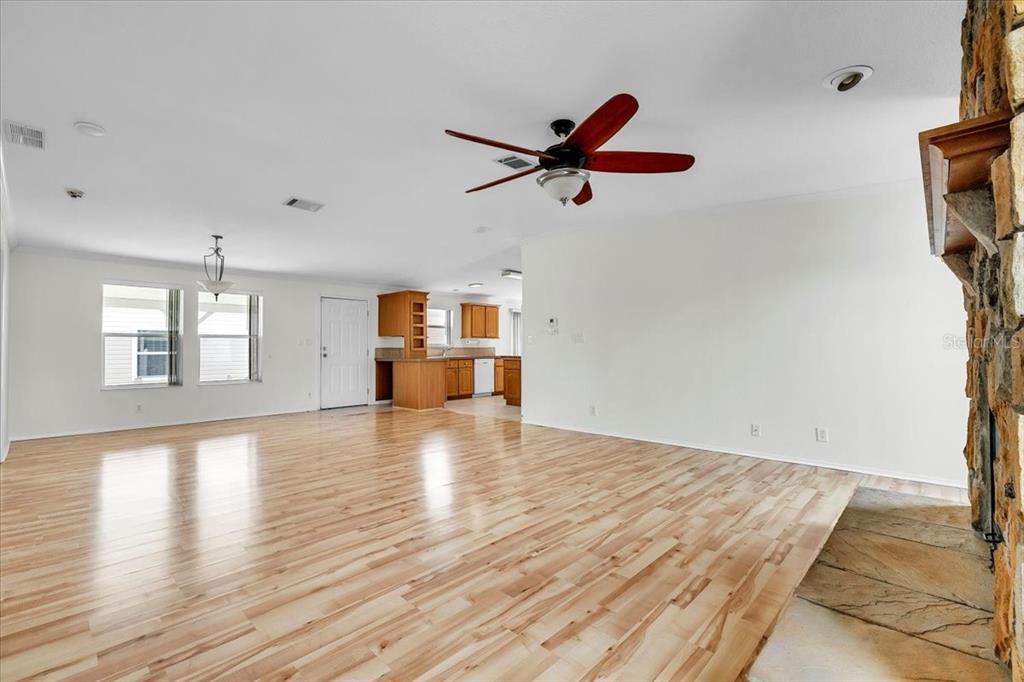 A spacious living room features light wood flooring, a ceiling fan, and a stone fireplace — 3650 ROSSMERE ROAD, PORT CHARLOTTE, FL