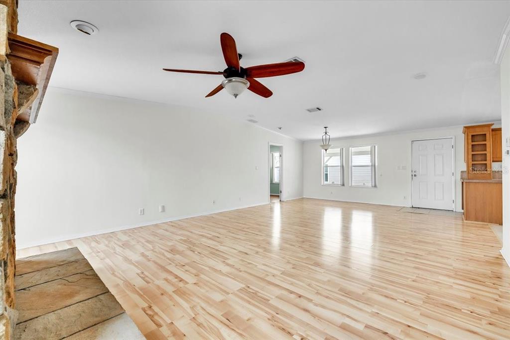 An open-concept living room features light wood flooring, a ceiling fan, and a stone fireplace — 3650 ROSSMERE ROAD, PORT CHARLOTTE, FL