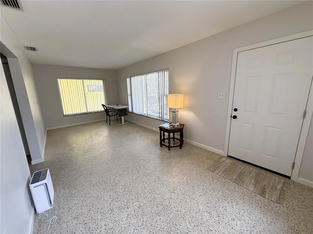 A living room features light-colored walls, terrazzo flooring, vertical blinds, and a white front door — 14017 W PARSLEY DRIVE, MADEIRA BEACH, FL