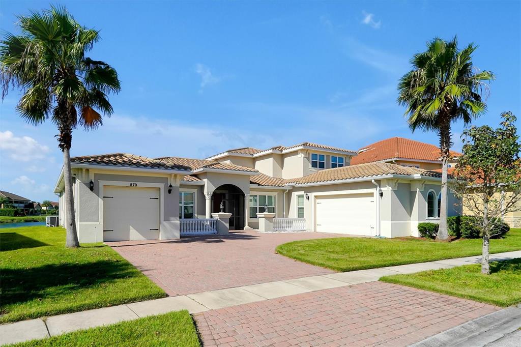 A two-story suburban house with a paver driveway, two garages, and two palm trees — 870 SPINNAKER WAY, KISSIMMEE, FL