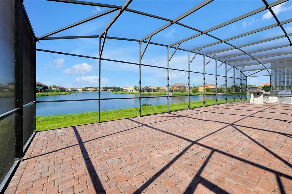 A screened-in brick patio overlooks a lake with houses in the background — 870 SPINNAKER WAY, KISSIMMEE, FL