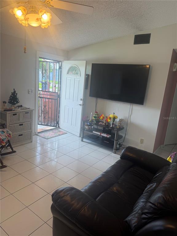 A living room with white tile floors, a ceiling fan, a television, and an entryway — 1304 DONWOODS LANE, ROYAL PALM BEACH, FL